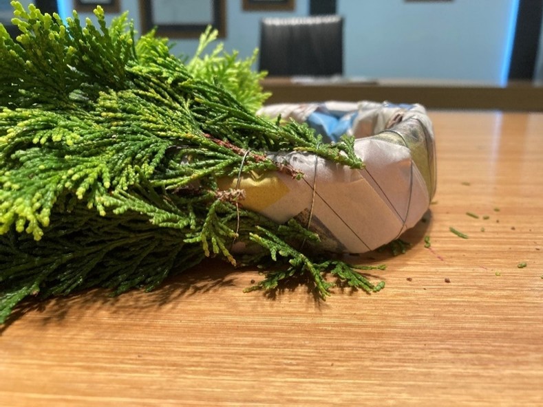 Small pieces of evergreen tree attached to a wheel of newspaper.