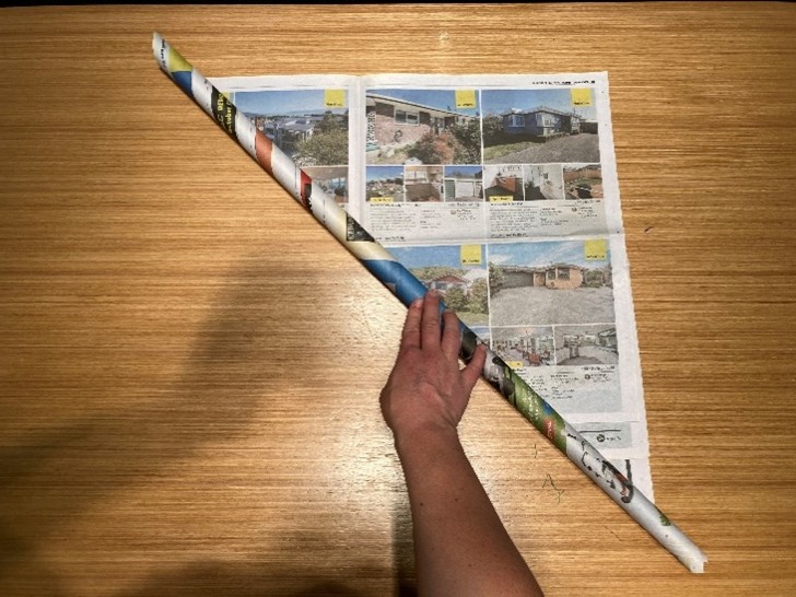 Newspaper being rolled into a tube diagonally.